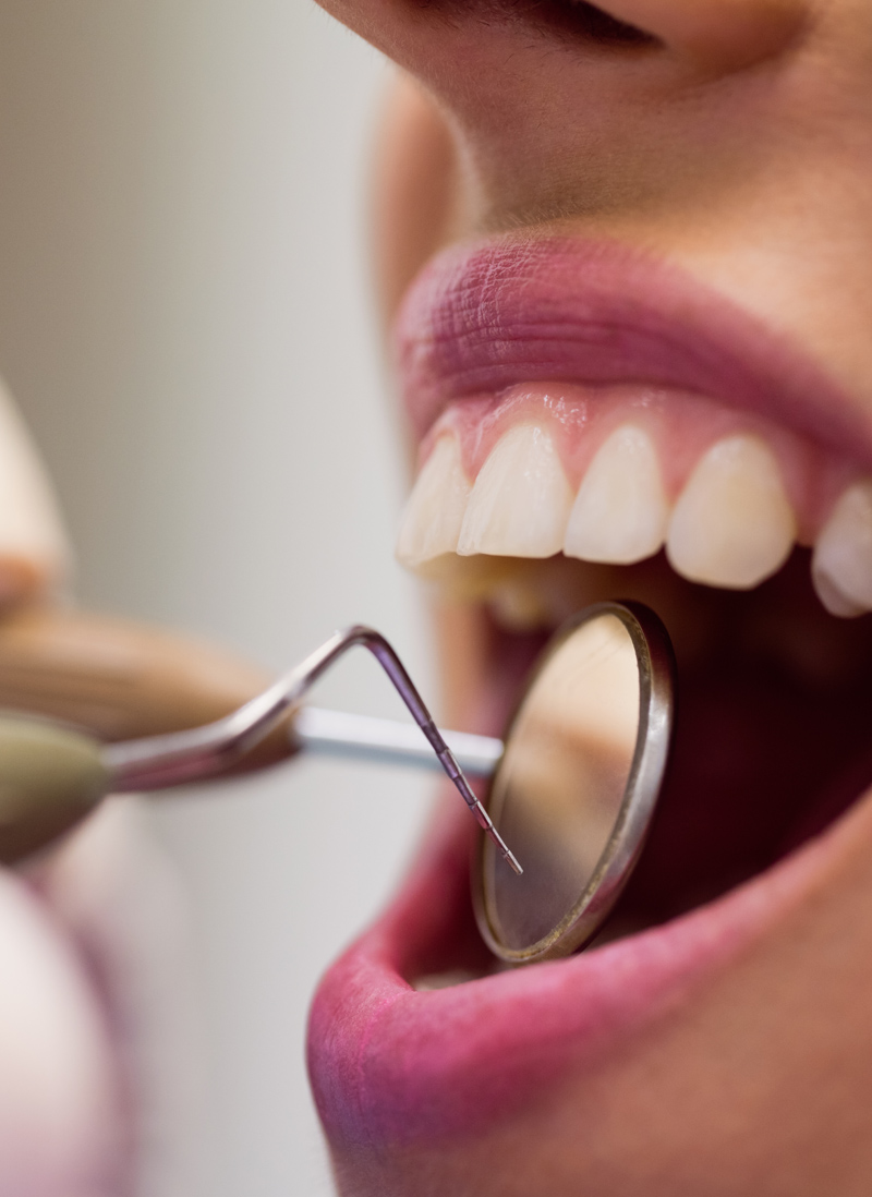 Close-up of dentist examining a female patient with tools at dental clinic